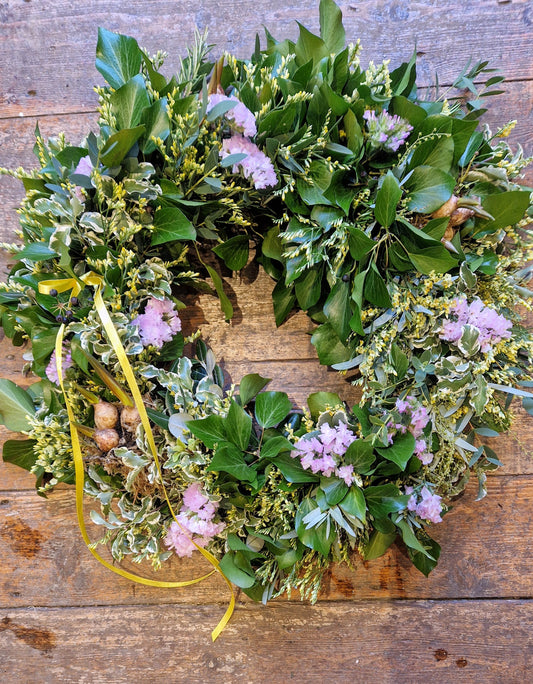 A freshly made spring wreath with green leaves and purple flowers, placed on a wooden surface.