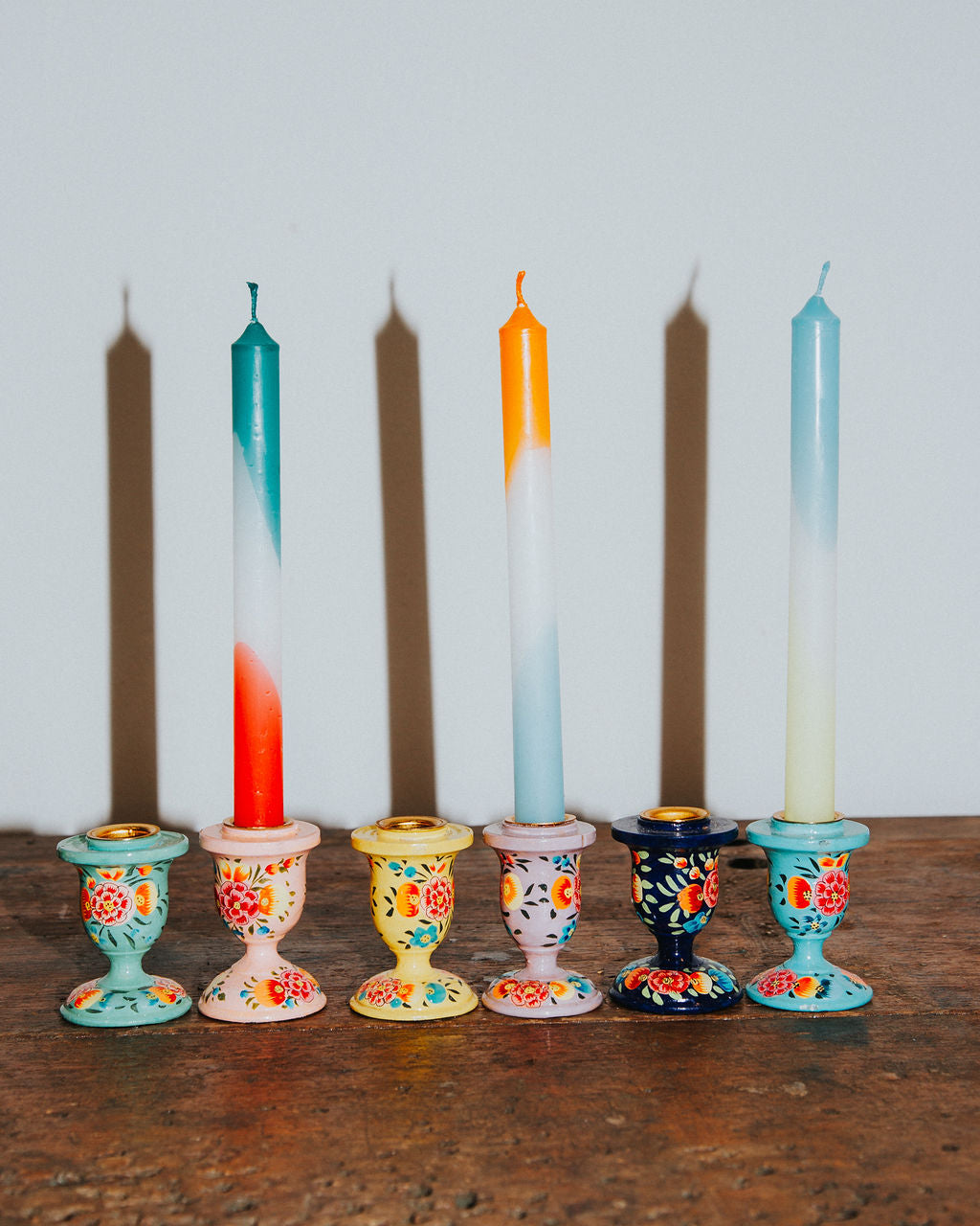 Colorful candles in decorative holders on a wooden surface with a white background