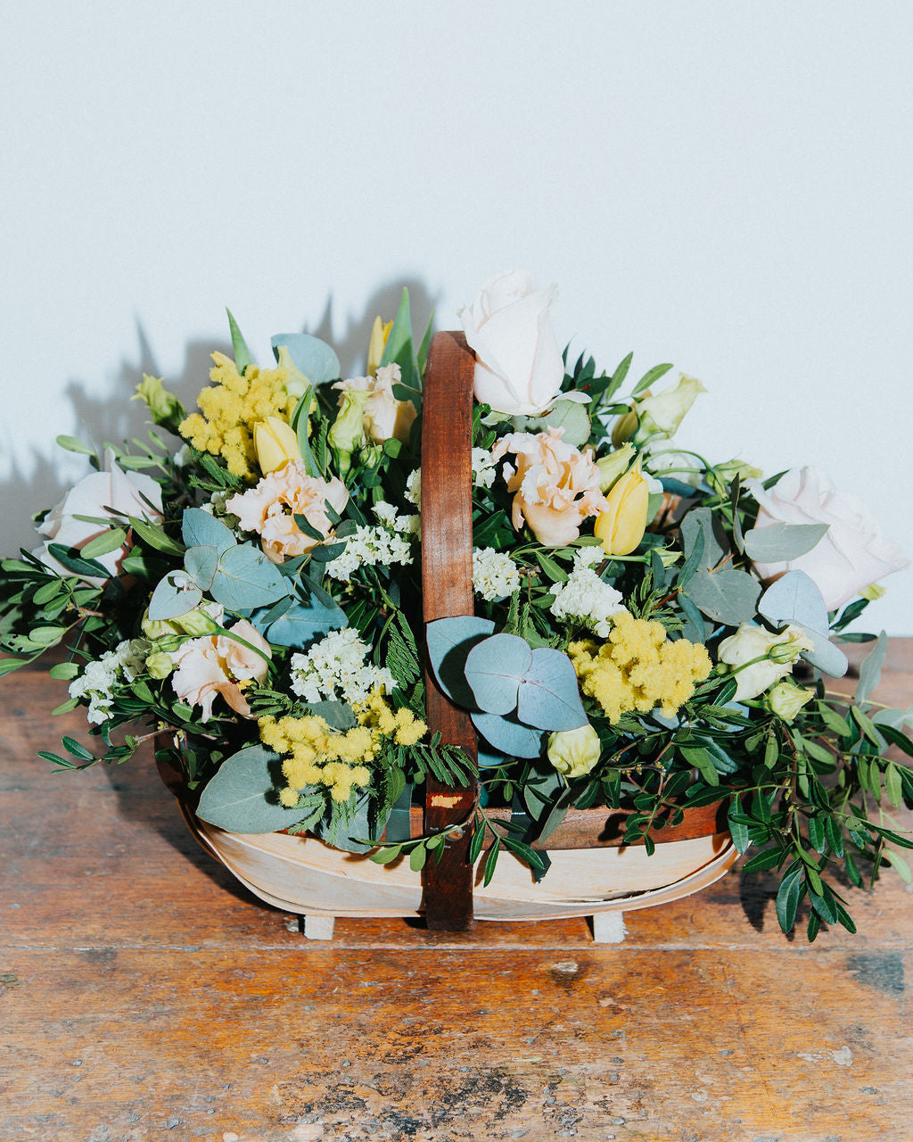 Floral arrangement in a woven basket on a wooden surface with a light blue background