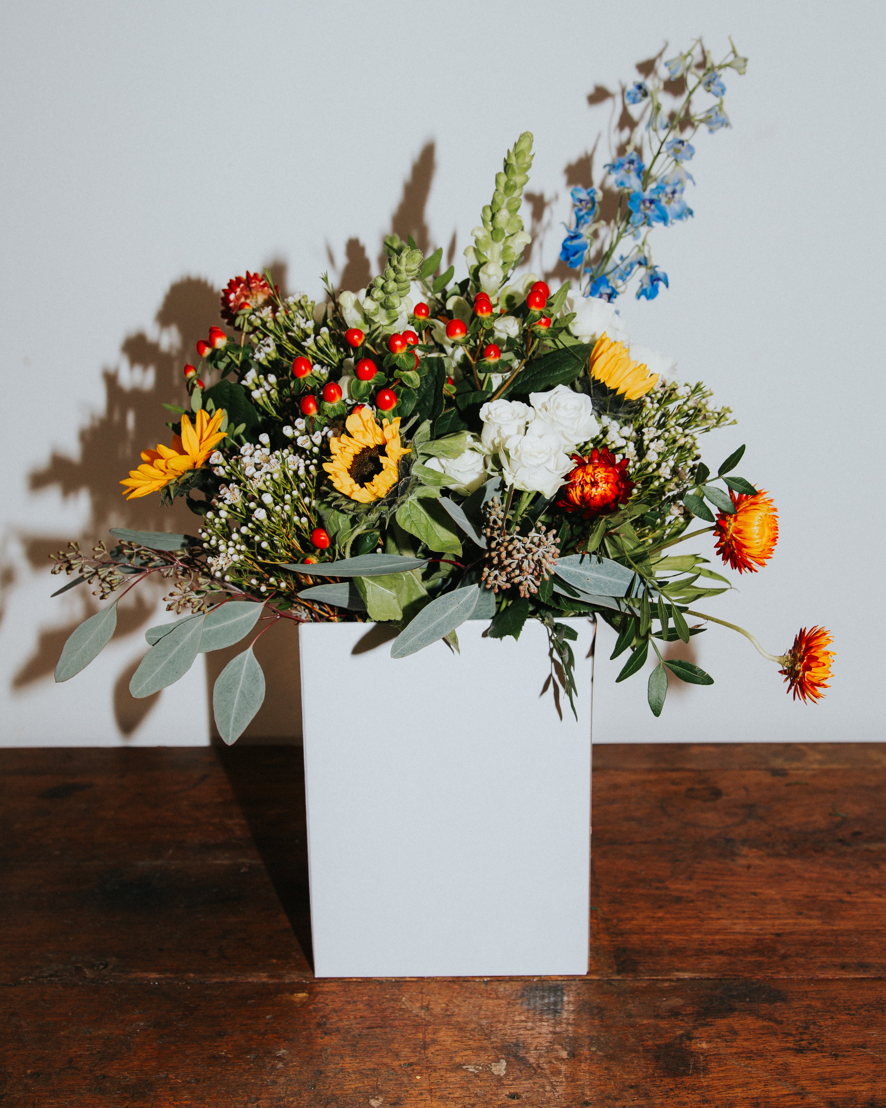 Colourful seasonal flowered up arrangement in a white box on a wooden surface with a neutral background